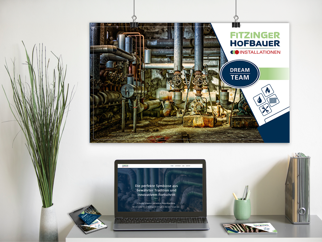 Blick auf einen Büro Arbeitsplatz mit Schreibtisch, darauf steht ein Laptop mit der Homepage der Firma Fitzinger Hofbauer. Links daneben ein Visitenkartenetui, rechts daneben Flyer und im Hintergrund ein große Werbetafel der Firma Fitzinger Hofbauer